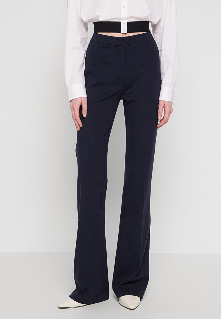 Marineblaue, taillierte Hose mit schlankem Schnitt und ausgestelltem Saum; aus einem glatten Stoff gefertigt; verfügt über einen hohen Bund und subtile Faltendetails.