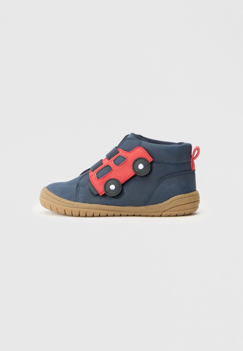 Marineblaue Kleinkinderschuhe mit hellbrauner Sohle und rotem Auto-Applikation an der Seite, das zwei schwarze Räder mit weißen Mitteln zeigt.