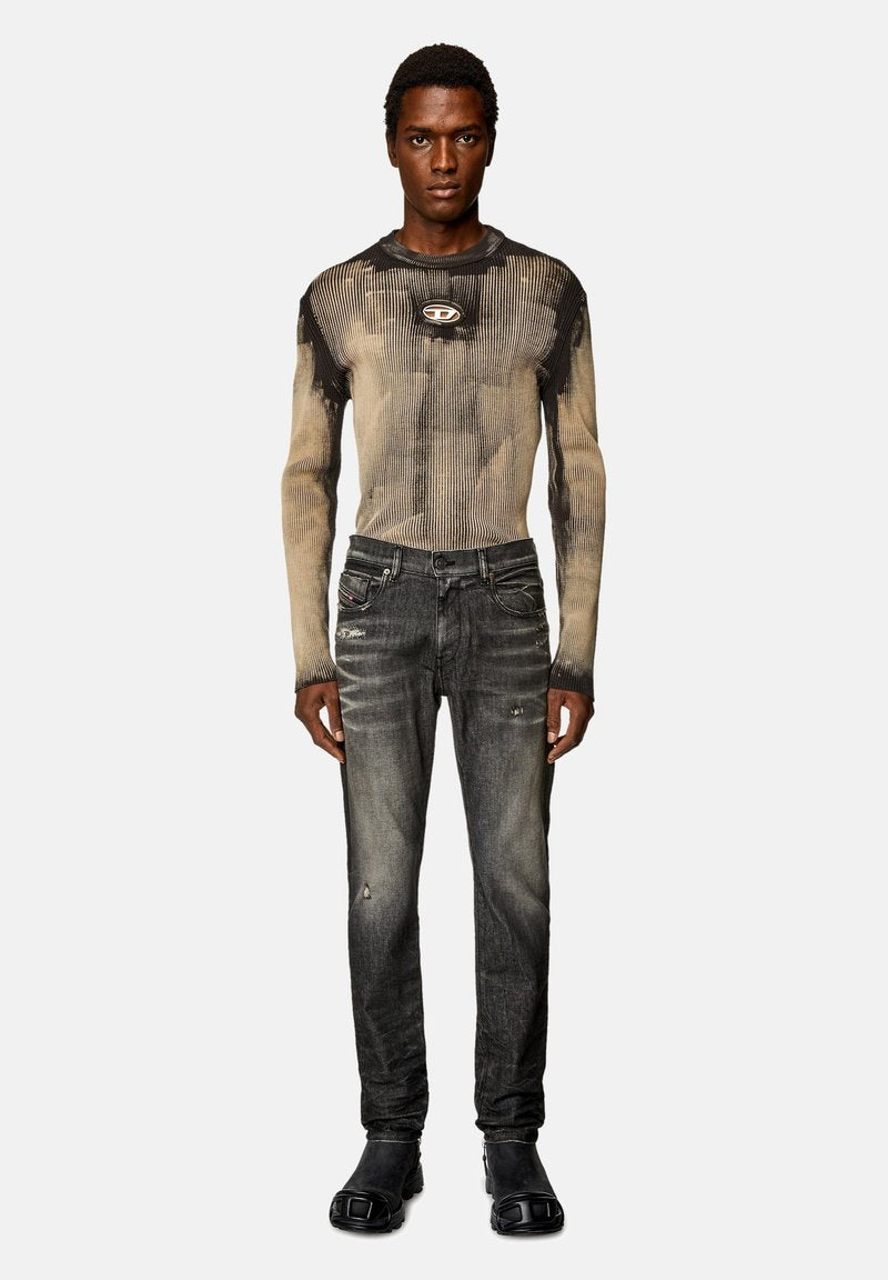 Langärmliges, geripptes Oberteil in Beige und Schwarz, kombiniert mit verblassten, ausgefransten, dunklen Jeans und schwarzen Stiefeln; das Shirt hat ein Logo-Detail.