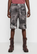 Schwarz-graue Denim-Shorts mit distressed Textur, die Risse und ein rotes Etikett aufweisen. Kombiniert mit dunkelbraunen Stiefeln. Lässiges Design.