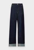 Dunkelblaue Jeans mit hoher Taille und weitem Bein, kontrastierenden umgeschlagenen Säumen und sichtbarer oranger Naht auf einfachem weißem Hintergrund.