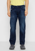 Dunkelblaue Jeans aus Denim mit geradem Schnitt, fünf Taschen, sanften Auswaschungen und einem Knopfverschluss. Getragen mit grauen Turnschuhen.