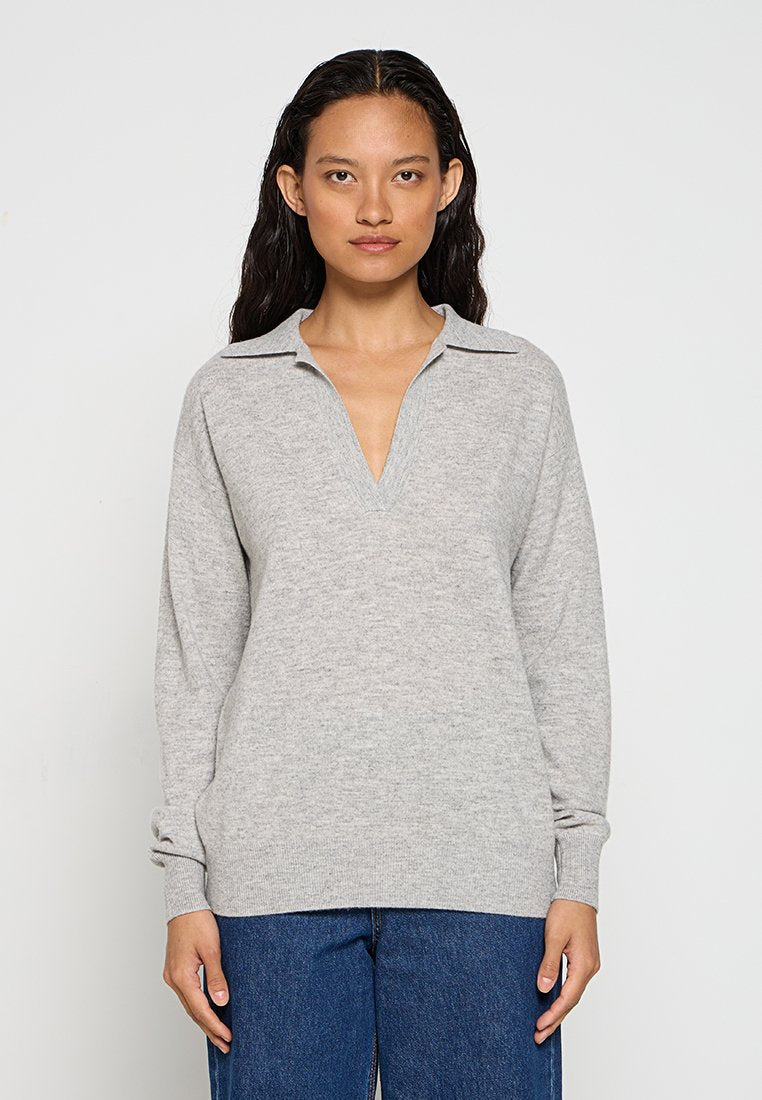 Grauer Strickpullover mit V-Ausschnitt und Kragen, langen Ärmeln und lockerer Passform. Glatte Textur, kombiniert mit blauen weit geschnittenen Jeans.