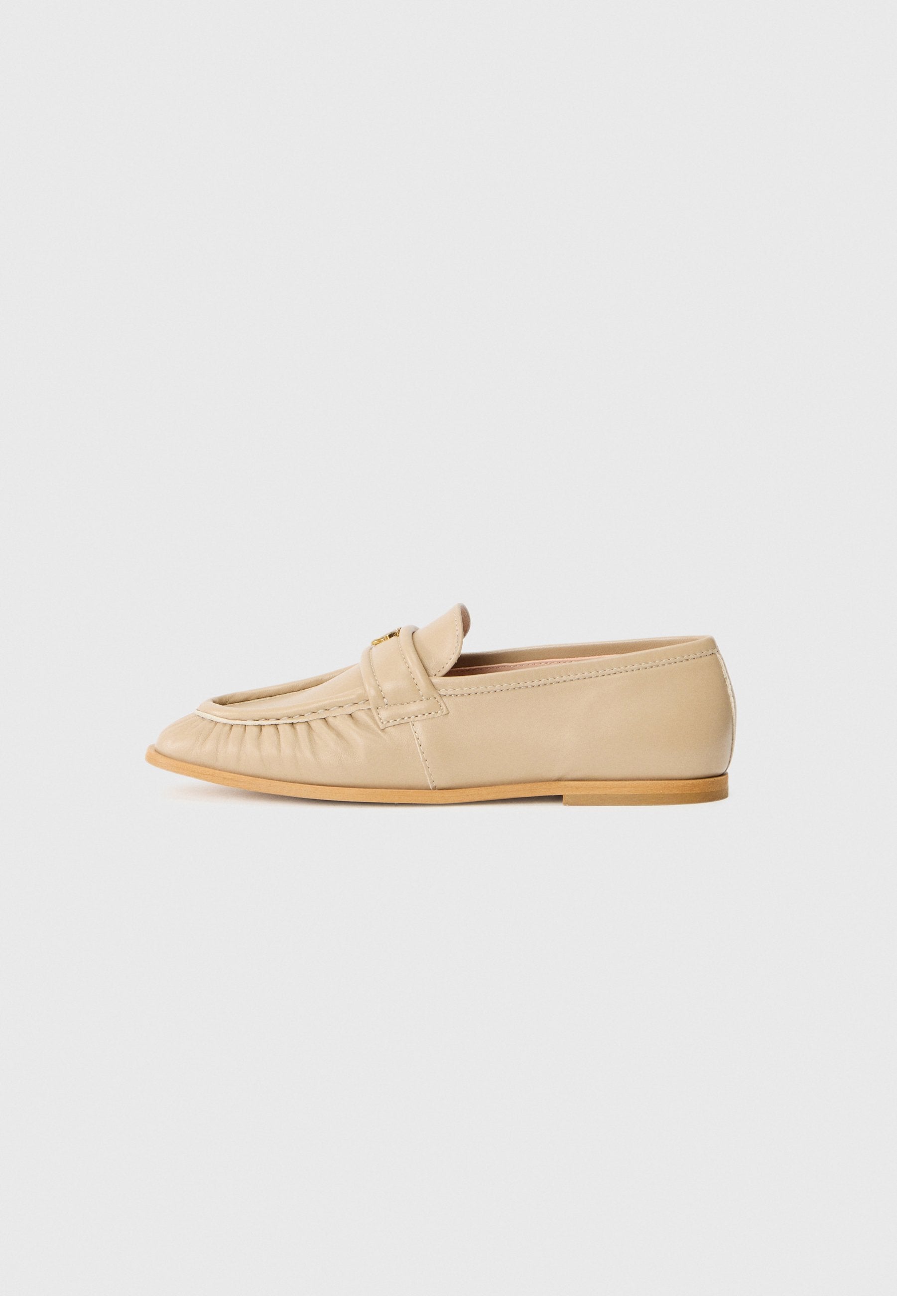 Beige Leder Slipper mit runder Zehenform, plissiertem Detail an der Vorderseite und einer tanfarbigen Gummisohle. Glatte Textur und minimale Hardware-Akzente.