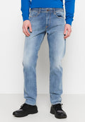 Mann trägt hellblaue, ausgewaschene Jeans, ein blaues Langarmshirt und schwarze Turnschuhe, steht mit entspannten Händen an den Seiten.