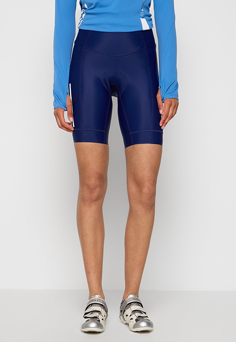 Marineblaue Radshorts mit enger Passform, ausgestattet mit Kontrastnähten und einem elastischen Bund. Kombiniert mit grauen Radschuhen.