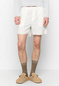 Weiße Baumwollboxershorts mit Knopfverschluss, elastischem Bund und seitlichen Schlitzen. Getragen mit beigen Slippers und braunen Socken.