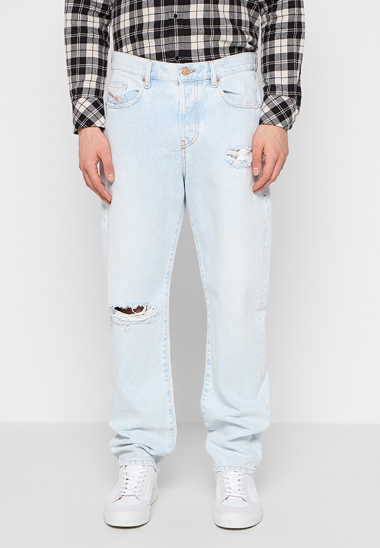 Hellblaue, zerrissene Jeans mit bequemer Passform, die eine abgenutzte Textur und Kontrastnähte aufweisen. Getragen mit weißen Sneakers und einem karierten Hemd.