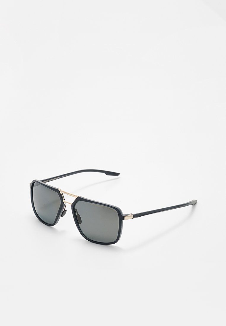 Schwarze Sonnenbrille mit quadratischen Gläsern, dünner goldener Metallbrücke und schwarzen Bügeln, die auf einer weißen Oberfläche liegen.