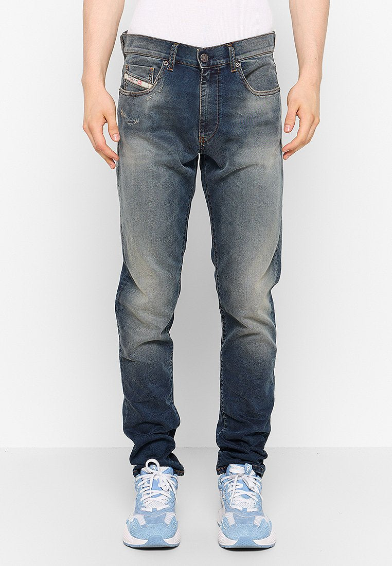 Blaue Denim-Jeans mit einem ausgewaschenen Effekt und leichten Abnutzungen. Verfügt über fünf Taschen und einen Knopfverschluss. Kombiniert mit hellblauen Sneakern.