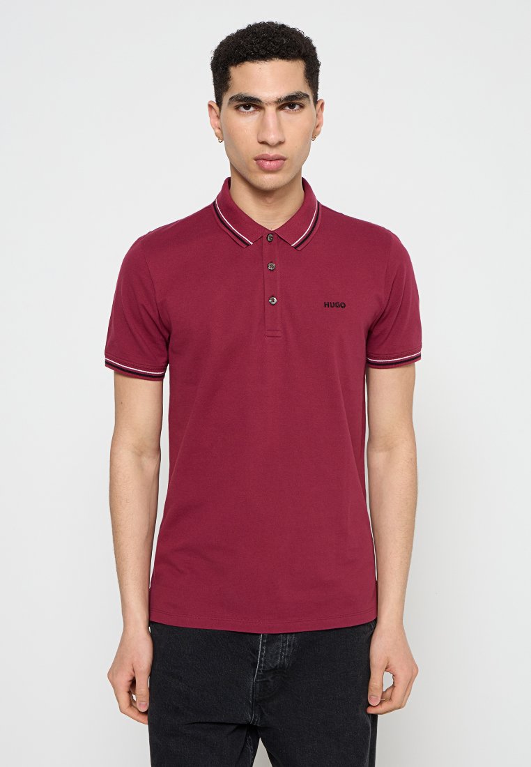 Burgunderfarbenes Poloshirt mit weißem und rotem gestreiftem Kragen, zwei Knöpfen und schwarzem Logo. Hergestellt aus weichem Baumwollstoff, taillierte Passform.