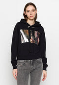 Schwarzer, gekürzter Hoodie mit einer silbernen, metallischen Vorderseite, Kordelzugkapuze und gerippten Bündchen. Kombiniert mit grauen Denim-Jeans.