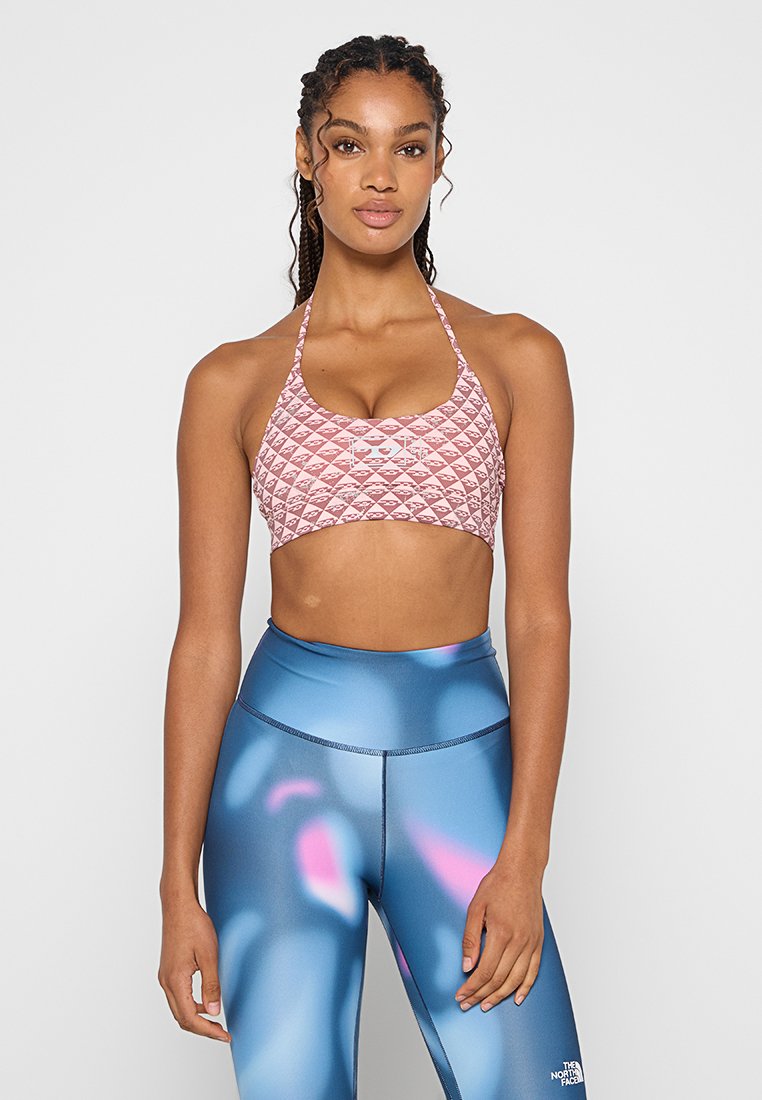 Sport-BH in Pink mit einem gesteppten Rautenmuster, kombiniert mit blauen Leggings, die abstrakte rosa und lila Akzente aufweisen. Glatte Stoffoberfläche.