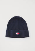 Marineblauer gestrickter Beanie mit gerippter Textur und umgeschlagenem Bündchen. Mit einem kleinen rechteckigen Logo-Patch in Rot, Weiß und Blau.