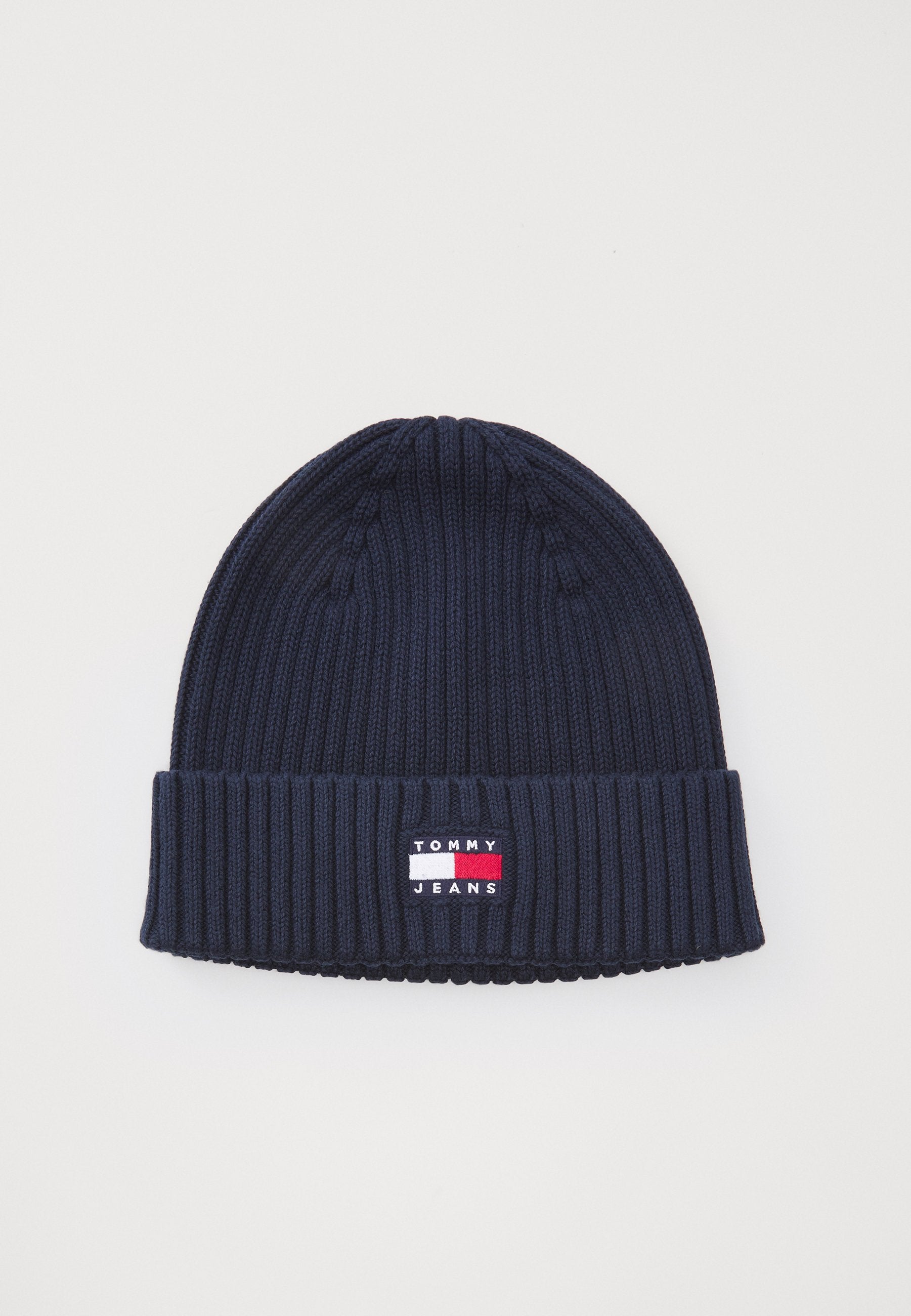 Marineblauer gestrickter Beanie mit gerippter Textur und umgeschlagenem Bündchen. Mit einem kleinen rechteckigen Logo-Patch in Rot, Weiß und Blau.