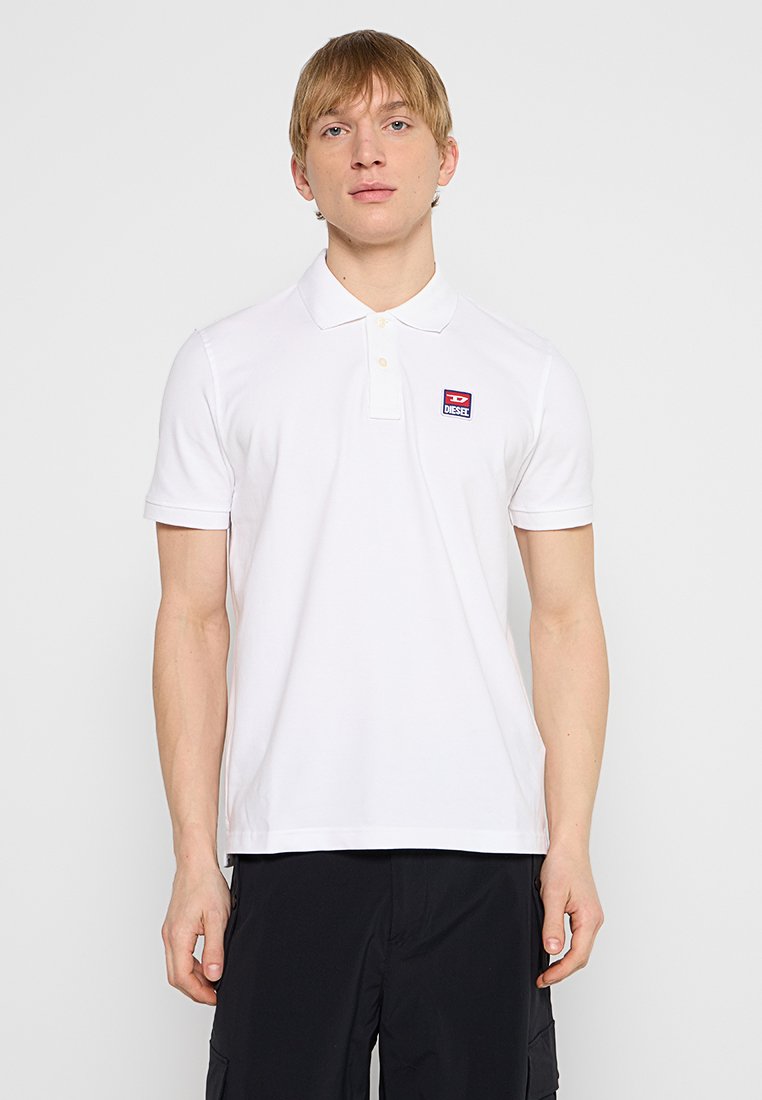Ein weißes Polohemd aus Baumwolle mit einem klassischen Kragen, kurzen Ärmeln und einem kleinen roten und blauen Markenlogo auf der linken Brust.