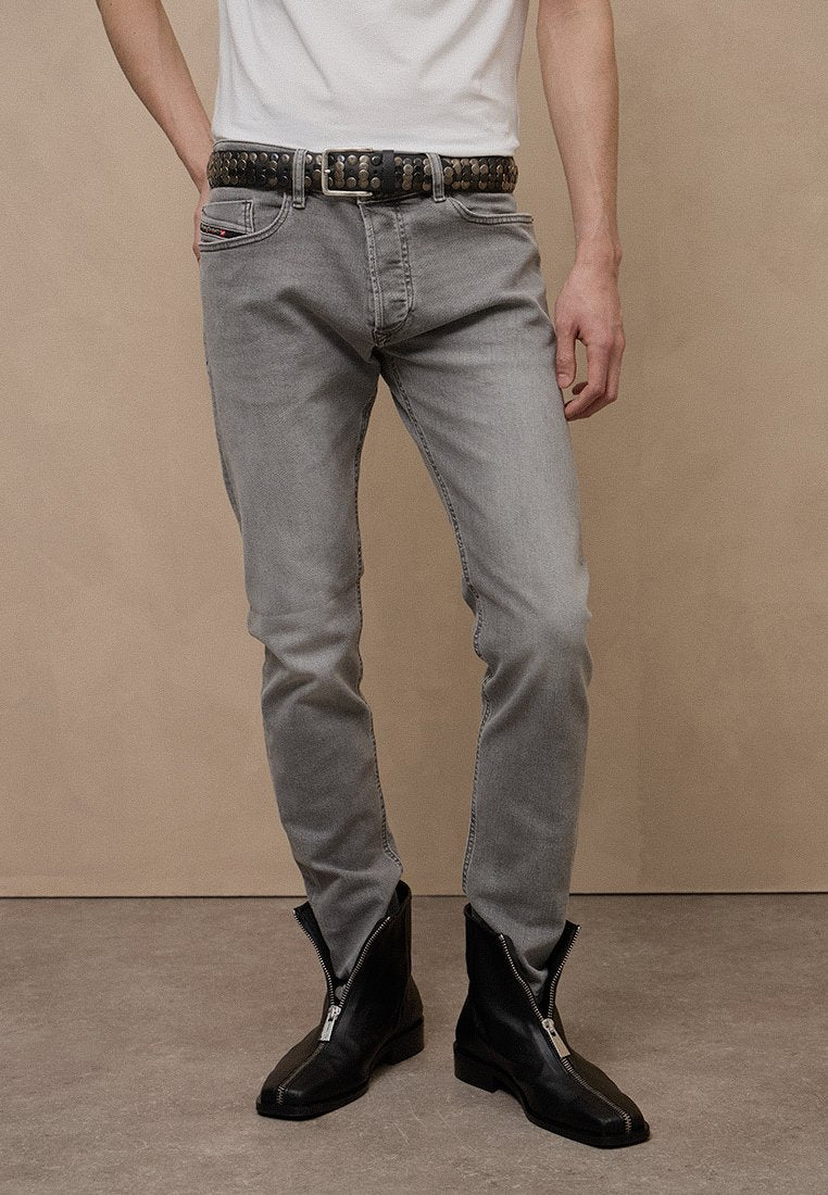 Graue Jeans mit schmaler Passform, strukturiertem Stoff und leichtem Used-Look. Kombiniert mit schwarzen Reißverschluss-Stiefeletten und einem schwarzen Nieten-Gürtel.