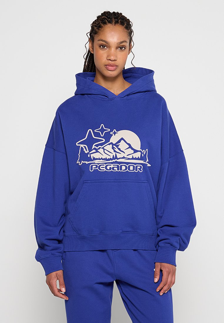 Blaues übergroßes Hoodie aus weichem Material, mit einer Kängurutasche und einem Bergmotiv mit Sonne und Sternen. Gerippte Bündchen und Saum.