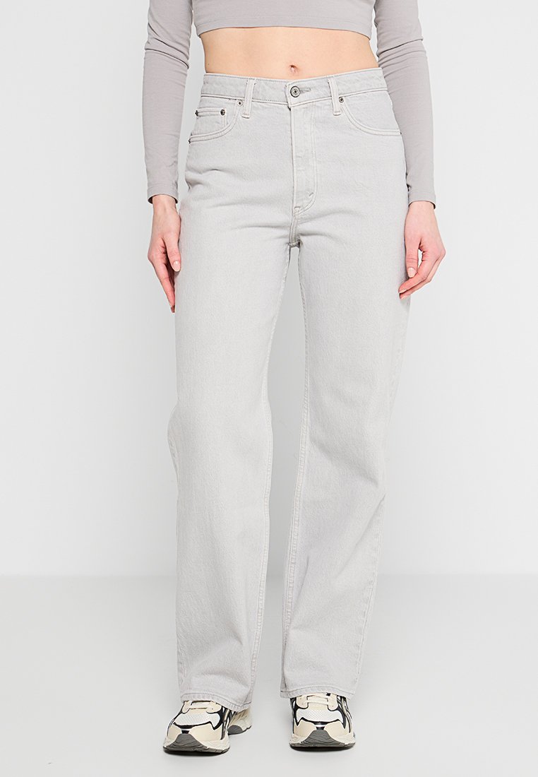 Helle graue High-Waisted-Jeans mit geradem Bein, minimalistischem Design und Fünf-Taschen-Styling. Kombiniert mit einem enganliegenden Crop-Top und Sneakers.