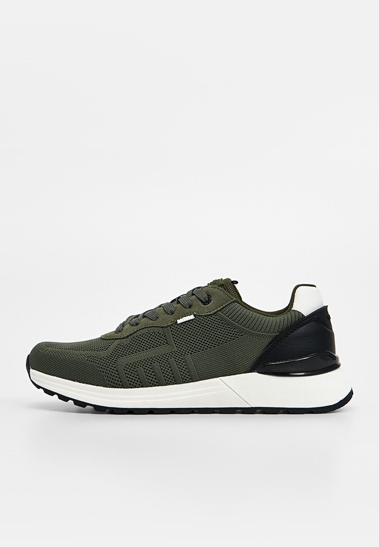 Olivgrüner Strick-Sneaker mit schwarzer Ferse, weißer Sohle und schwarzer Laufsohle, von der linken Seite vor einfachem Hintergrund gezeigt.