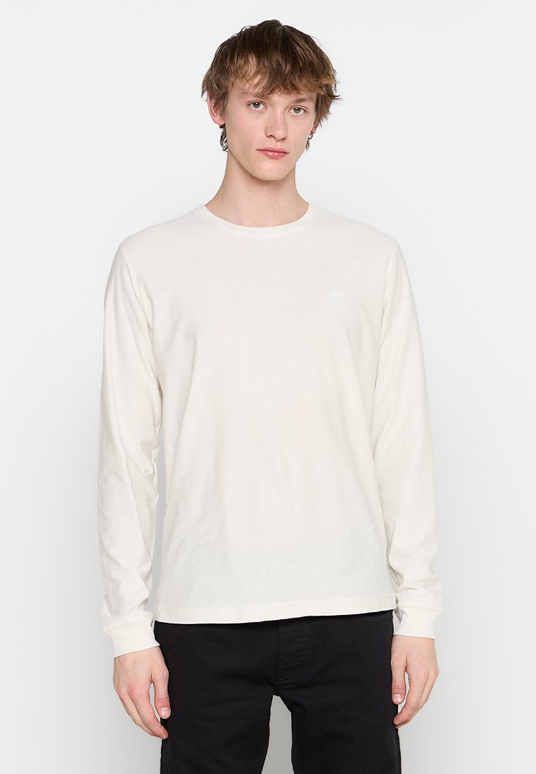 Langärmliges, cremefarbenes Baumwoll-T-Shirt mit rundem Halsausschnitt und kleinem Logo auf der Brust. Weicher Stoff und lockere Passform.