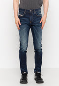 Mann in dunkelblauen Slim-Fit-Jeans mit ausgebleichten Details und schwarzen Sneakern, steht vor einem schlichten weißen Hintergrund.