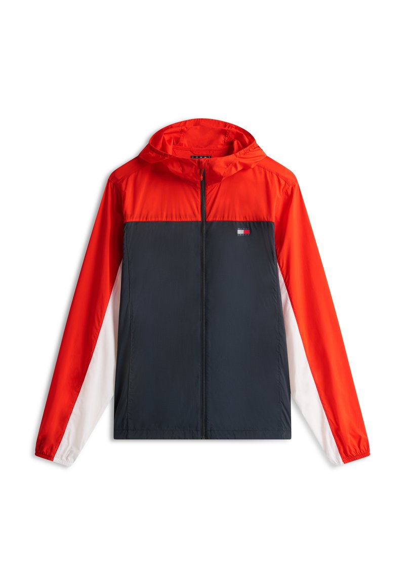 Kinder-Windjacke mit Kapuze in rotem Oberteil, navyblauem Mittelteil und weißen unteren Ärmeln, mit kleinem Logo auf der Brust.