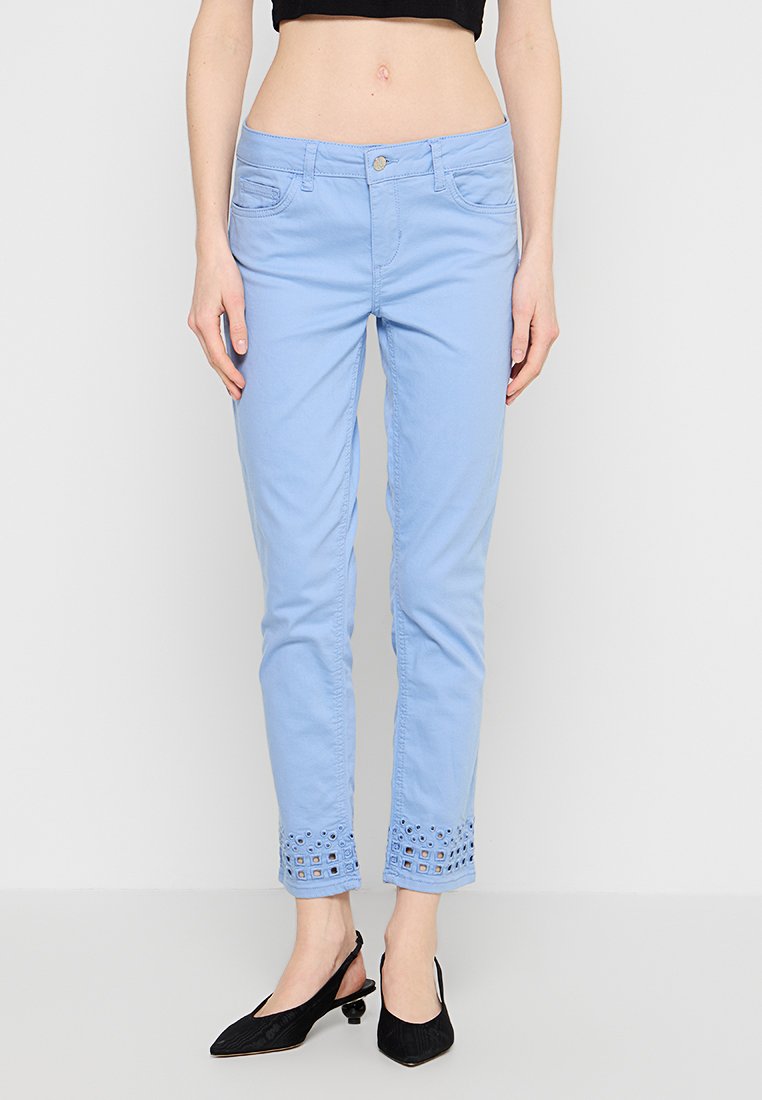 Hellblaue Slim-Fit-Hosen mit Lochmuster-Details an den gekürzten Säumen, kombiniert mit schwarzen Slippern mit niedrigem Absatz.