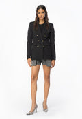 Schwarzes doppelt geknöpftes Blazer mit goldenen Knöpfen, getragen über einem schwarzen Oberteil, kombiniert mit grauen Denim-Shorts und High Heels im Schlangenprint.