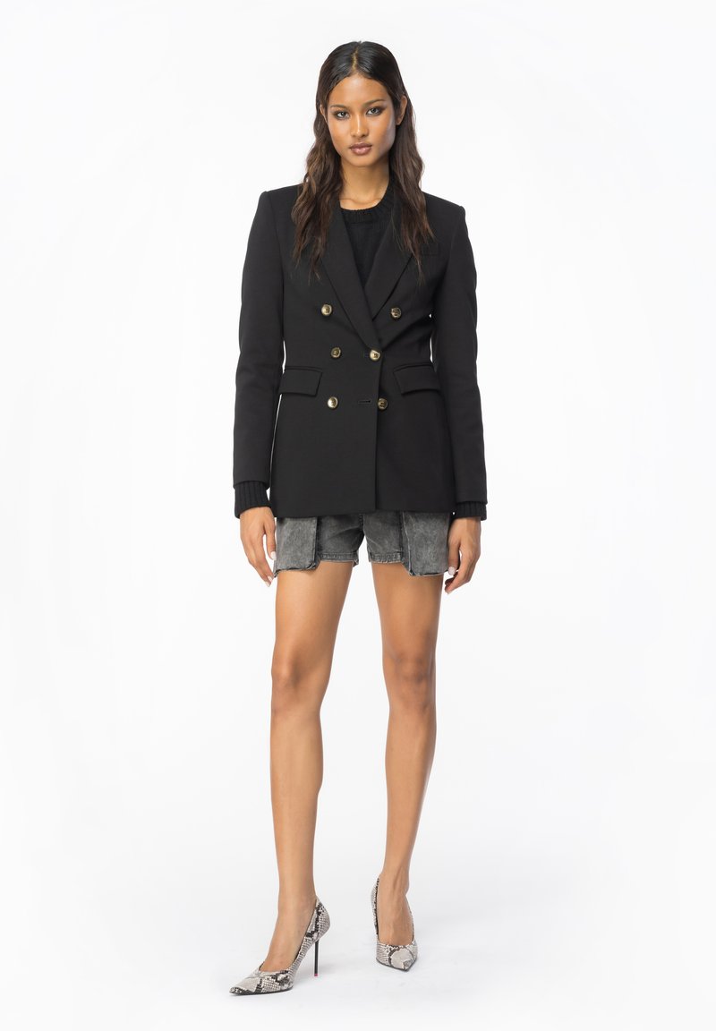 Schwarzes doppelt geknöpftes Blazer mit goldenen Knöpfen, getragen über einem schwarzen Oberteil, kombiniert mit grauen Denim-Shorts und High Heels im Schlangenprint.
