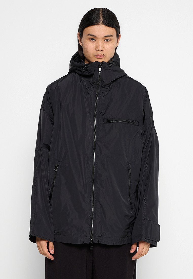 Schwarze Kapuzenjacke aus leichtem, wasserabweisendem Material. Mit vorderem Reißverschluss, zwei seitlichen Taschen und einer Brusttasche.