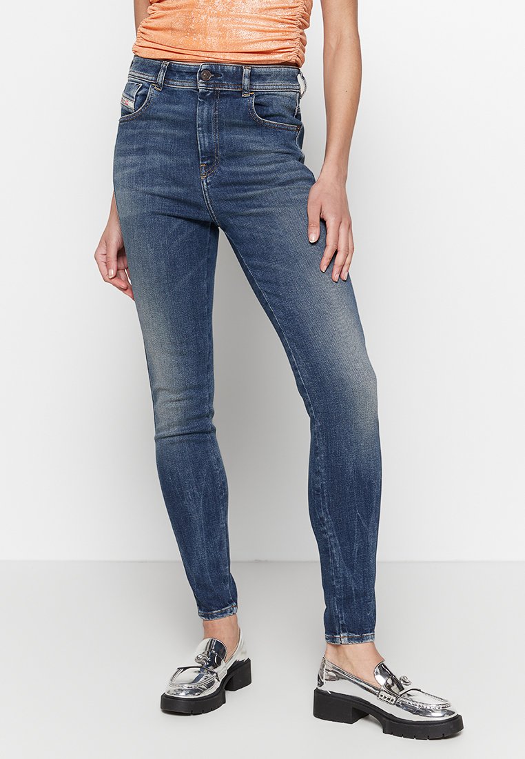 Schlanke Jeans aus dunkelblauem Denim mit einem verblassten Finish, ausgestattet mit fünf Taschen, Gürtelschlaufen und einem vorderen Knopfverschluss. Kombiniert mit silbernen Loafers.