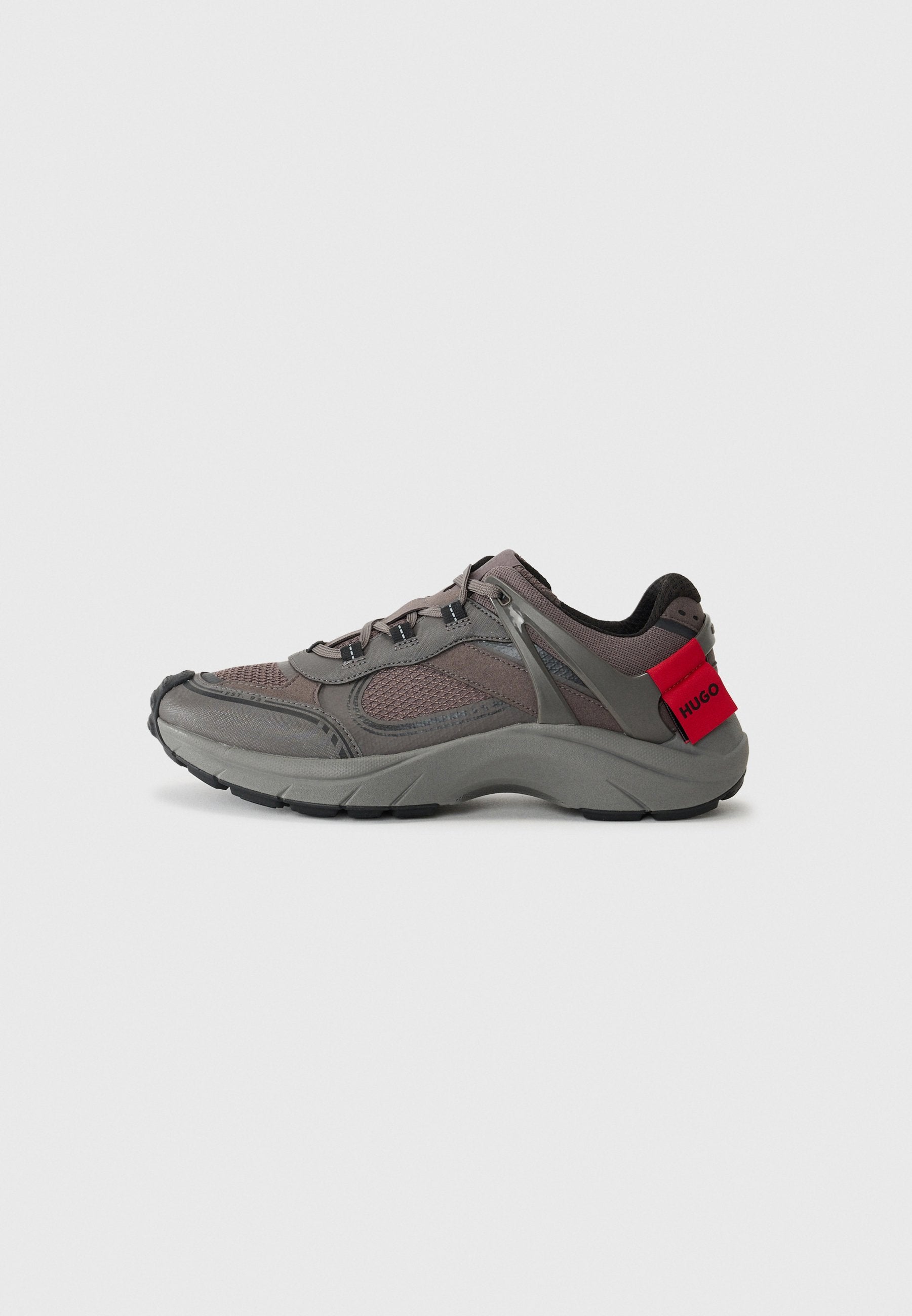 Graue Sportschuhe mit Obermaterial aus Mesh, schwarzen Akzenten und roter Fersenschlaufe. Mit Schnürsenkeln und strukturiertem Sohlenprofil für besseren Halt. Modernes Design.