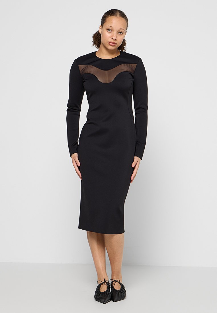 Schwarzes, figurbetontes Kleid mit langen Ärmeln, das ein durchscheinendes Netzpaneel am Ausschnitt hat. Knielang, glatte Textur, schlichtes Design.
