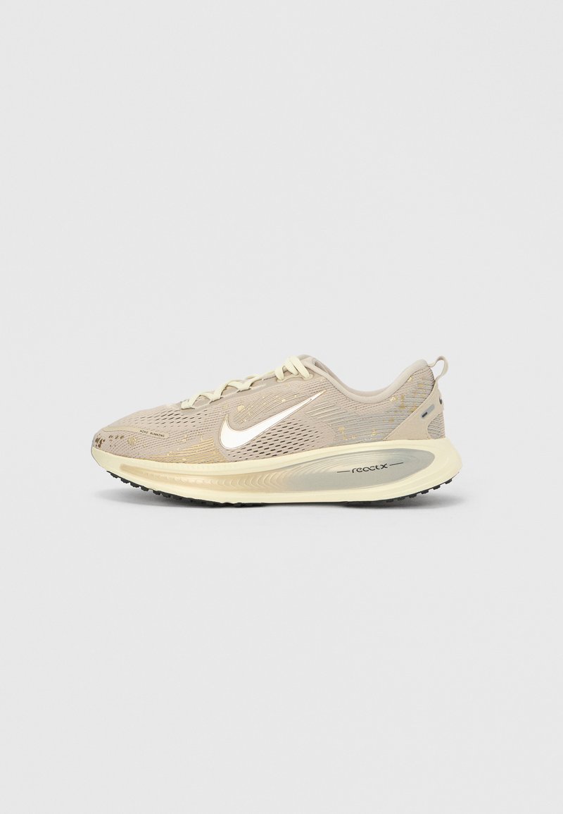 Beiger Nike Laufschuh mit weißem Swoosh-Logo, cremefarbener Sohle mit der Aufschrift "react" und atmungsaktivem Mesh-Obermaterial mit goldenen Akzenten.