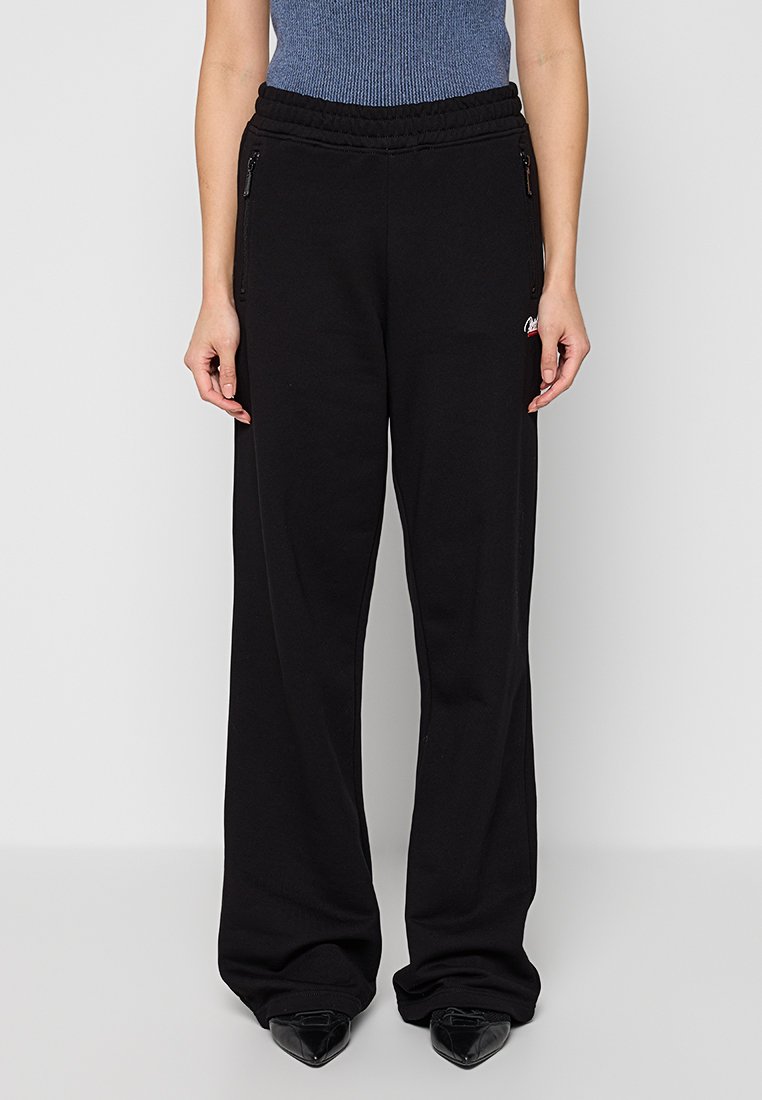 Schwarze, weit geschnittene Sweatpants mit einem elastischen Bund, zwei Reißverschlusstaschen und einem kleinen Logo-Detail an der linken Hüfte. Weicher, entspannter Schnitt.