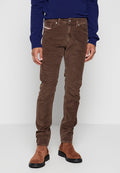 Braune Cordhosen mit schmaler Passform, ausgestattet mit Vordertaschen, einem Knopfverschluss und subtiler Textur. Getragen mit einem blauen Pullover und braunen Schuhen.