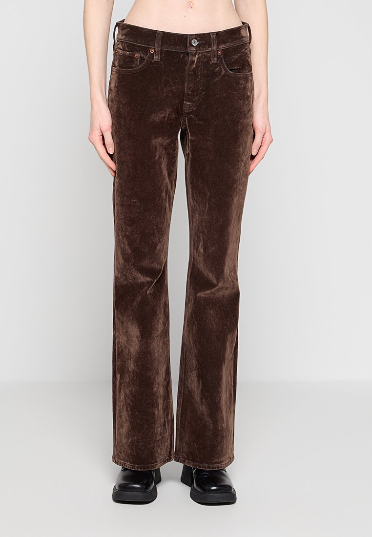 Dunkelbraune Samthose mit geradem Bein, getragen mit schwarzen Schuhen, gezeigt von der Taille bis zu den Füßen vor einem schlichten hellen Hintergrund.