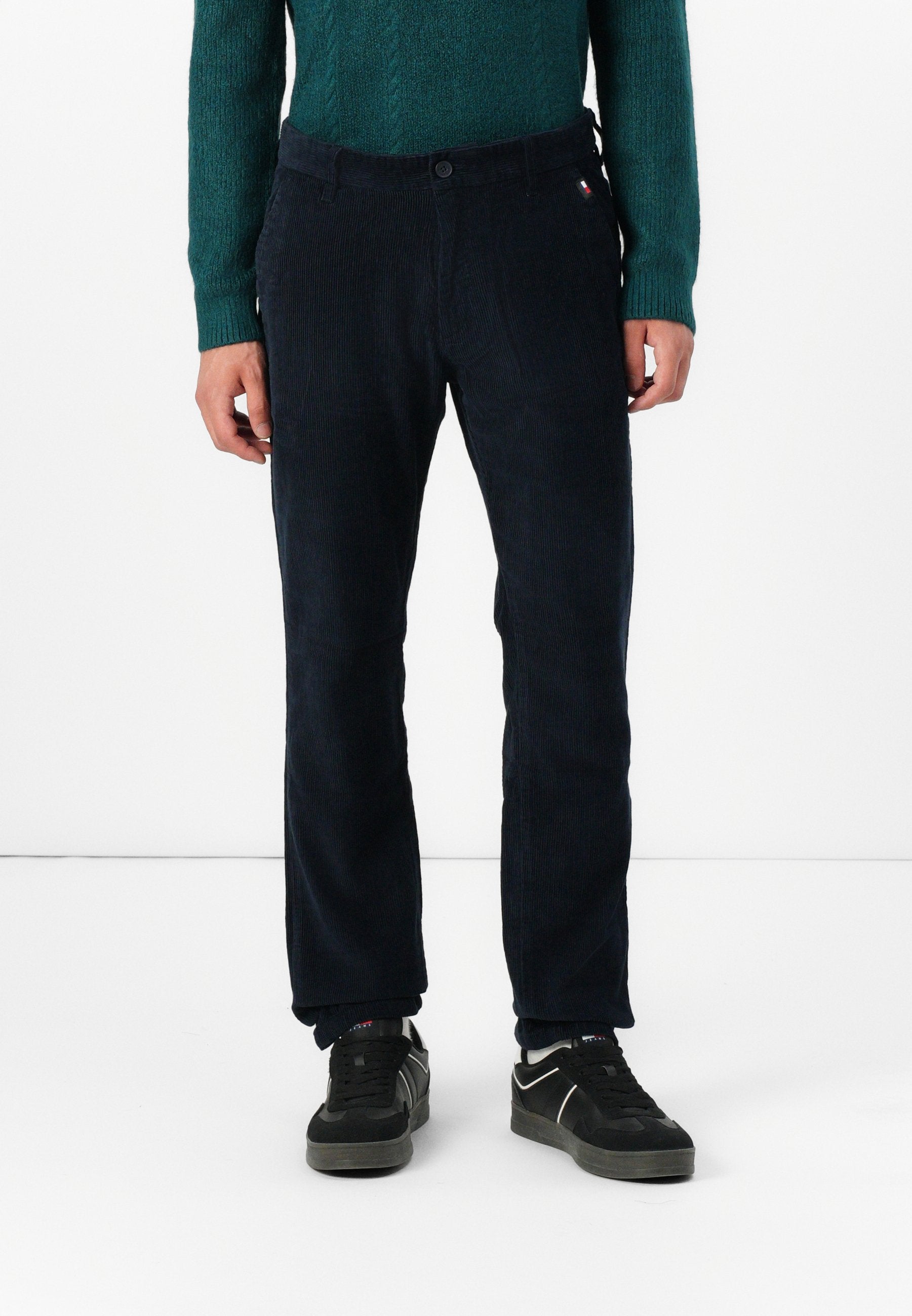 Marineblaue Cordhosen mit normaler Passform, Knopfverschluss, dezentem Muster und seitlichen Taschen. Getragen mit schwarzen Sneakers.