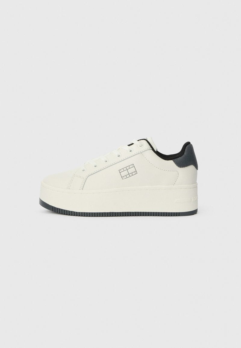 Weißer Sneaker mit einer leicht erhöhten Plattform, glatter Textur, schwarzen Akzenten an der Ferse und einem Logo an der Seite.