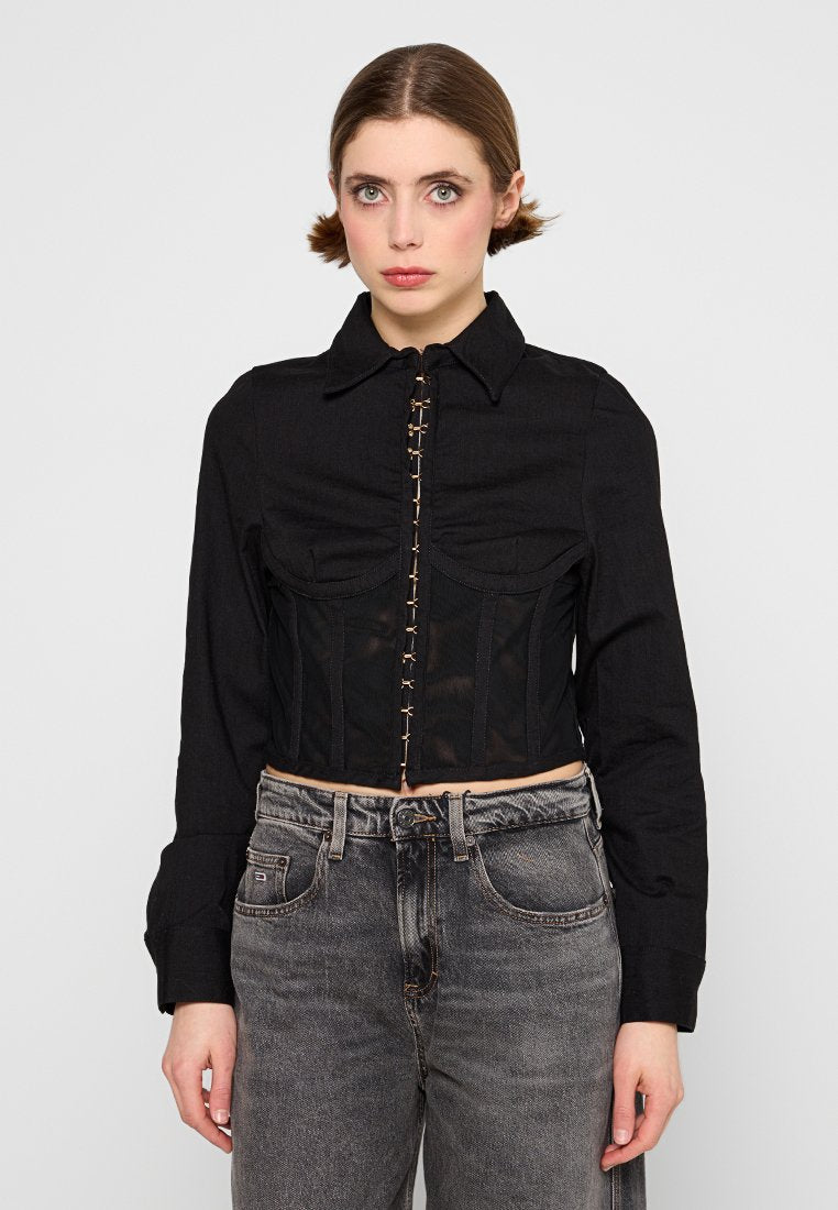 Schwarze, kurz geschnittene Jacke mit Kragen und Knopfverschluss, die durchscheinende Einsätze und ein strukturiertes Design des Oberteils aufweist. Getragen mit grauen Jeans.
