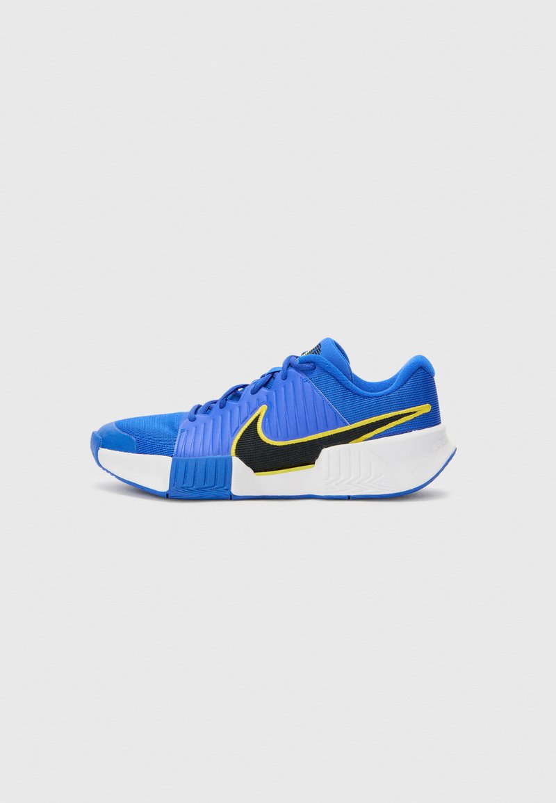 Blaue Sportschuhe mit strukturiertem Obermaterial, einem schwarzen Nike-Swoosh, gelben Akzenten und einer weißen Gummisohle. Sie verfügen über eine runde Zehenform und ein Schnürdesign.