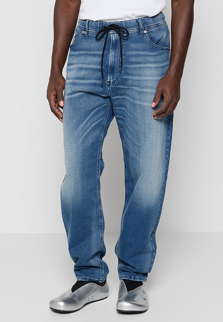 Blaue Jeans aus Denim mit lockerem Schnitt, Kordelzugbund, heller Verwaschung und Taschen vorne sowie hinten. Kombiniert mit silberfarbenen Slip-On-Schuhen.