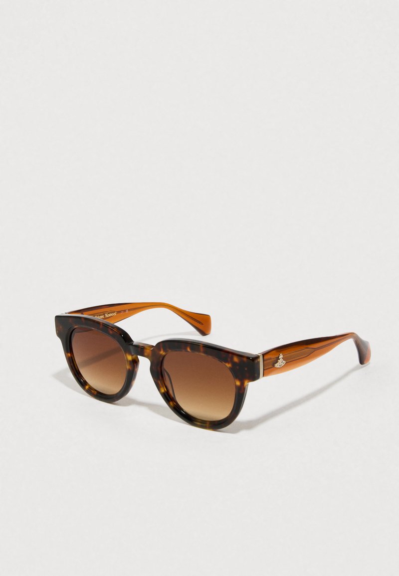 Schildpatt-Sonnenbrille mit verlaufenden braunen Gläsern, geometrischer Katzenaugenform und orangefarbenen Akzenten an den Bügeln mit einem Metallschriftzug.
