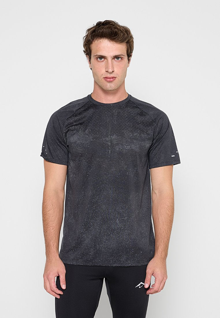 Junger Mann trägt ein schwarzes kurzärmeliges Sportshirt und schwarze Hose, steht mit Blick nach vorne vor einem schlichten hellen Hintergrund.