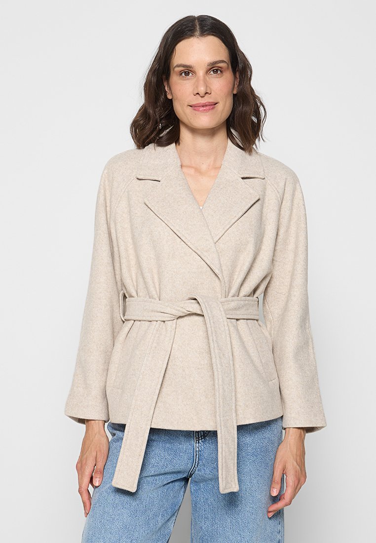 Beige Wickeljacke aus weichem Stoff, mit einem Taillengürtel, breiten Revers und langen Ärmeln. Mit einer subtilen Textur.