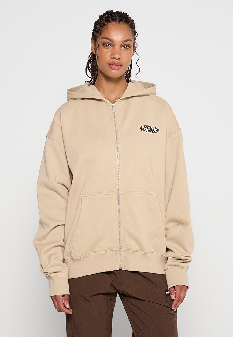 Beige Zip-Up-Hoodie aus weichem Baumwollmaterial. Verfügt über eine große Fronttasche und ein Logo auf der linken Brust. Enthält eine Kapuze mit Kordelzug und einen lockeren Schnitt.