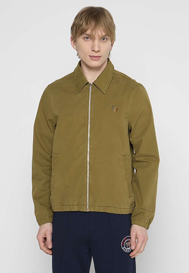 Olivgrüne Zip-Jacke mit spitzem Kragen, elastischem Bund, seitlichen Taschen und kleinem gesticktem Logo auf der Brust. Glatte Textur.