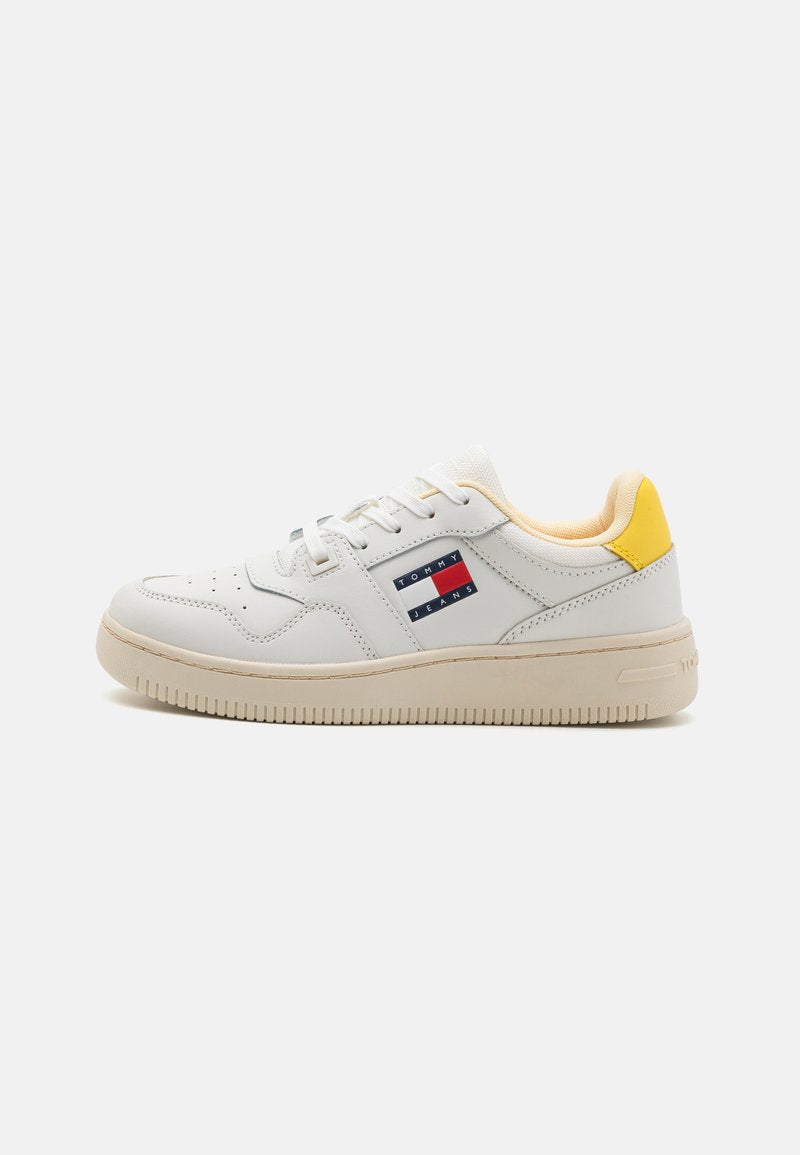 Weißes Leder-Sneaker mit beiger Sohle, ausgestattet mit buntem Logo-Patch, gelbem Akzent an der Ferse und Standard-Schnürsenkeln. Glatte Textur über das gesamte Schuhwerk.