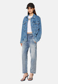 Denimjacke in Hellblau, lockere Passform mit Fronttaschen. Weißes Crop-Top darunter, ausgewaschene blaue Jeans und schwarze Cap. Riemchen-Pumps.